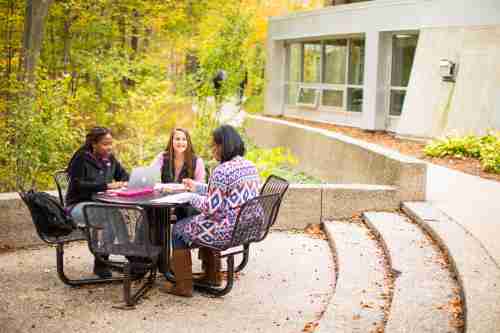 Contemporary photo of students sitting at a round table on the back side of the Traditional Housing buildings, by the ravine